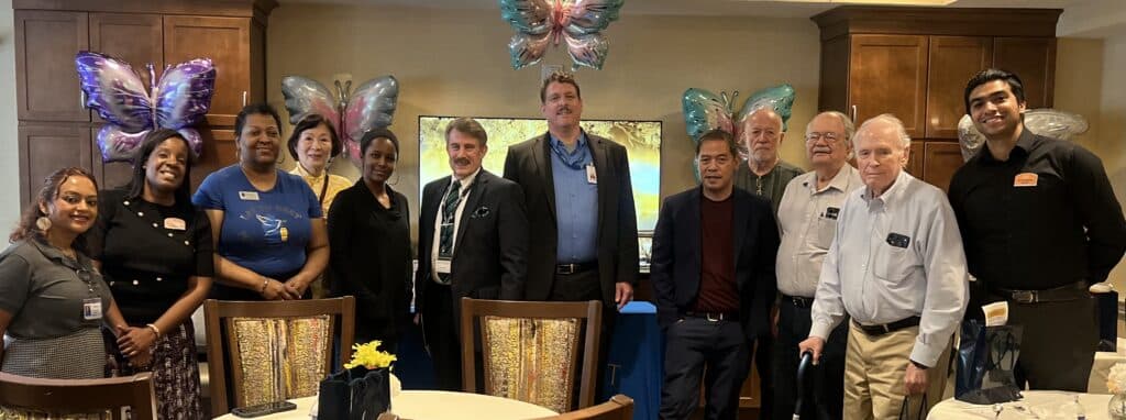 Group of coworkers posing for a photo at a celebration, with butterfly balloons in a dining room behind them.
