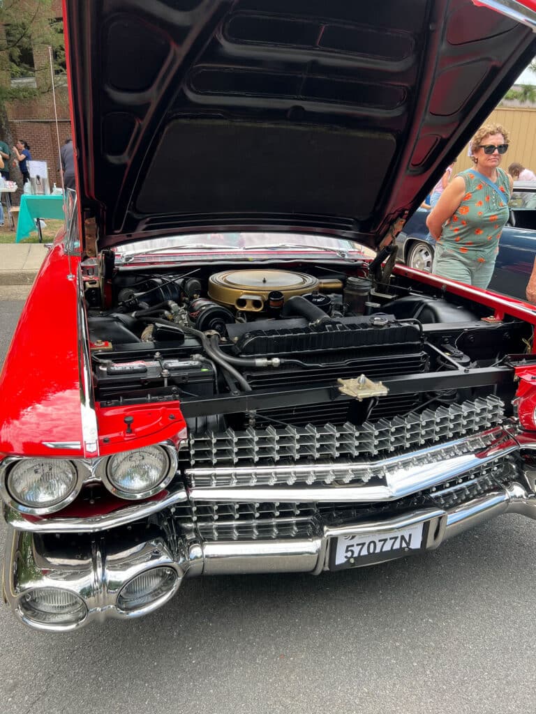 Red vintage car with hood up, engine bay visible at a car show; license plate 57077N in front.